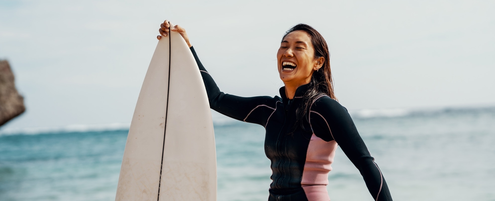 Excited woman in a wetsuit holding surfboard on the beach